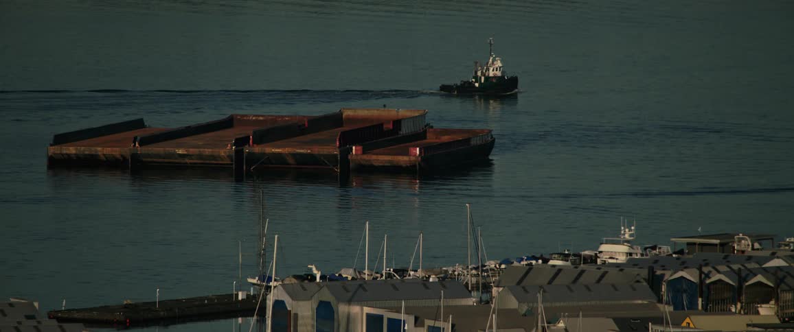 Boat cruises through water past platform a short distance from marina and warehouses