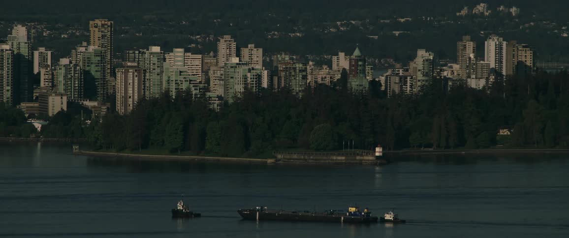 A tugboat drags a barge across a river in front of a city skyline