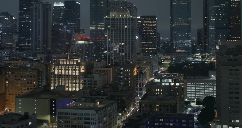 Traffic drives along street through downtown passing lit buildings at night