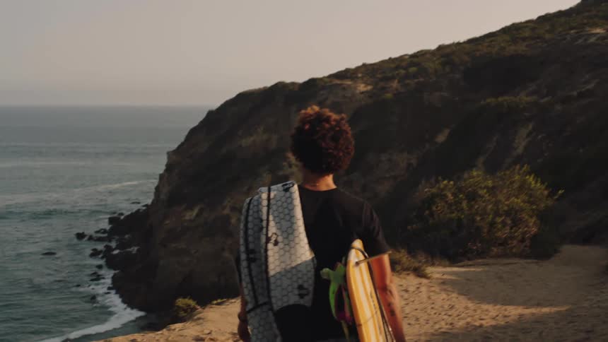 A woman carrying a surfboard and a towel over his shoulder walking towards the beach