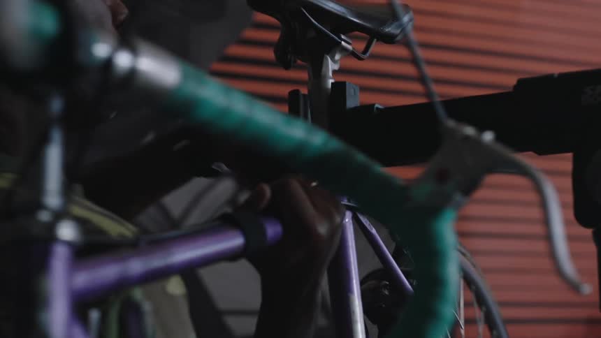 A close up of a man placing his bicycle on on a bar clamp and fastening it tight so it hangs