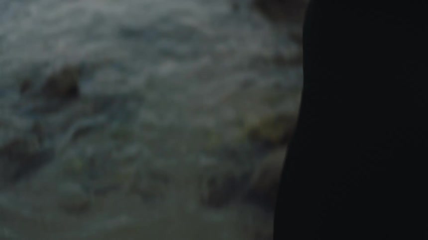 The backside of a woman putting on a wet suit standing in front of the ocean