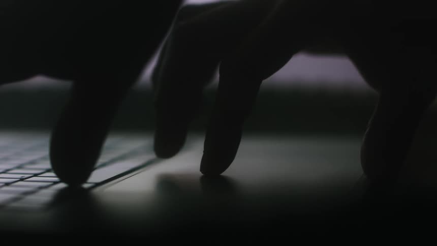 A person uses the touchpad on a laptop in a dimly lit room