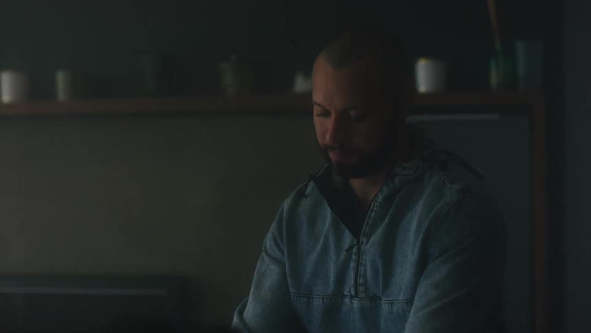 Bearded man wearing a denim jacket carrying a laptop then sitting down and opening the lid