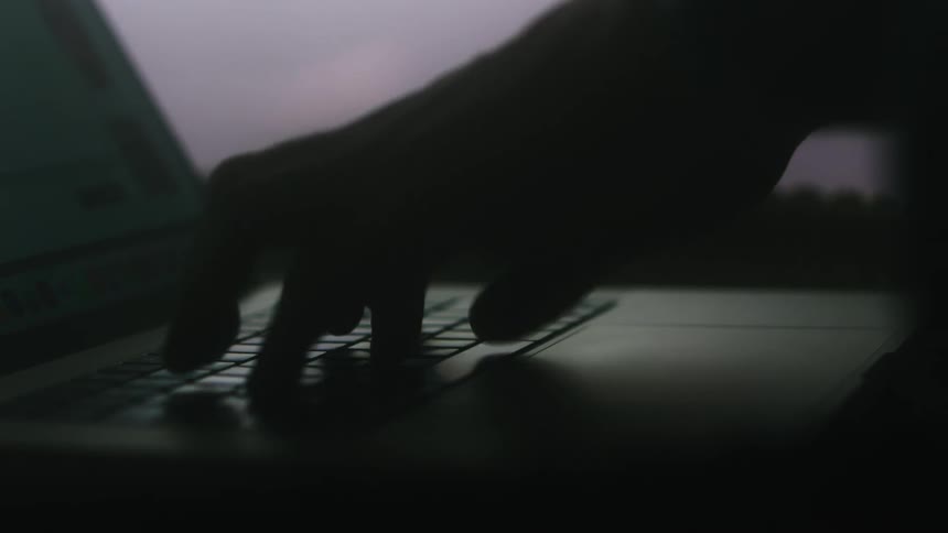 A person types on a laptop in a dimly lit room