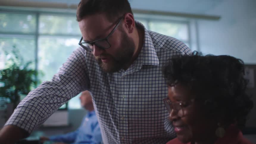 Woman smiles as her coworker points to her computer screen and offers feedback