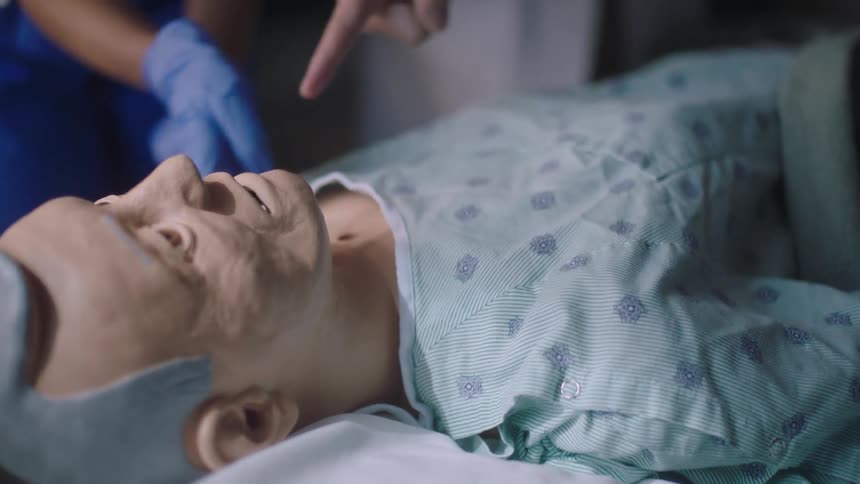 Nurses are touching a dummy man dressed in a gown on a hospital bed
