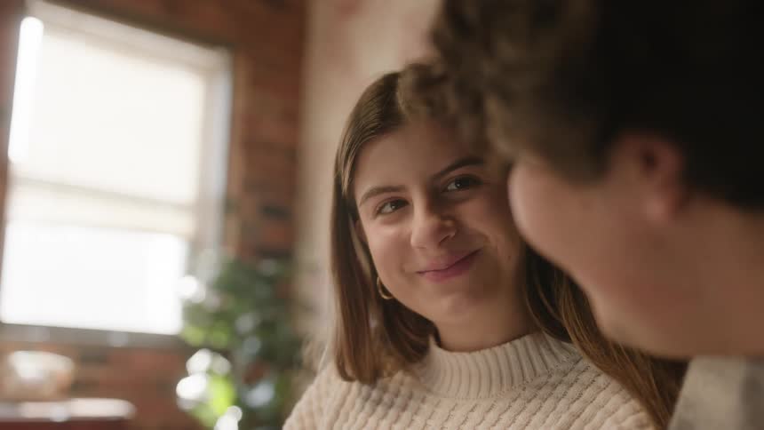 A close up of a womans face as she looks at the man next to her and smiles at him before looking down