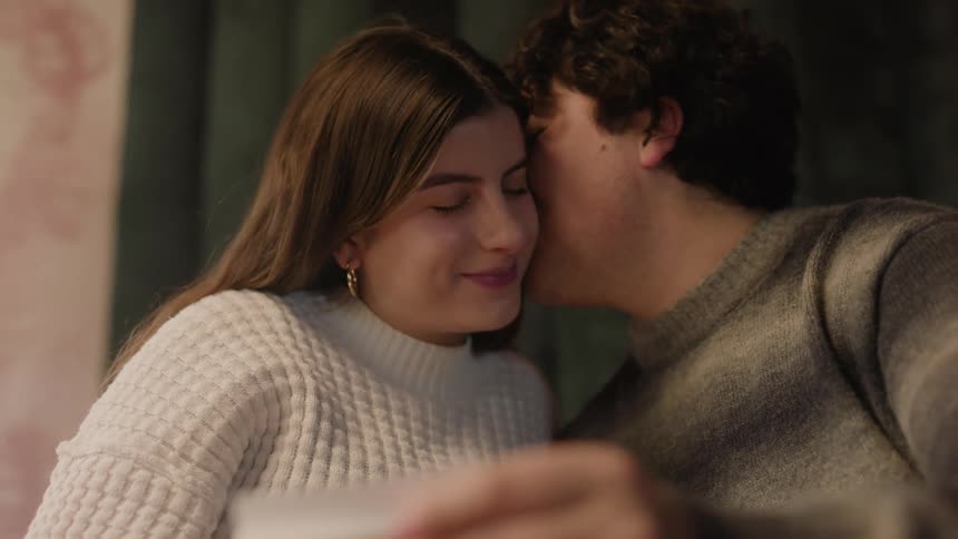Close up of a man and woman sitting together when the man kisses the woman on the cheek