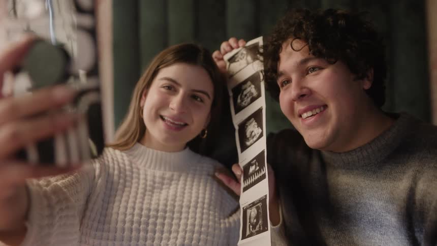 A man and woman holding up photos of a sonogram