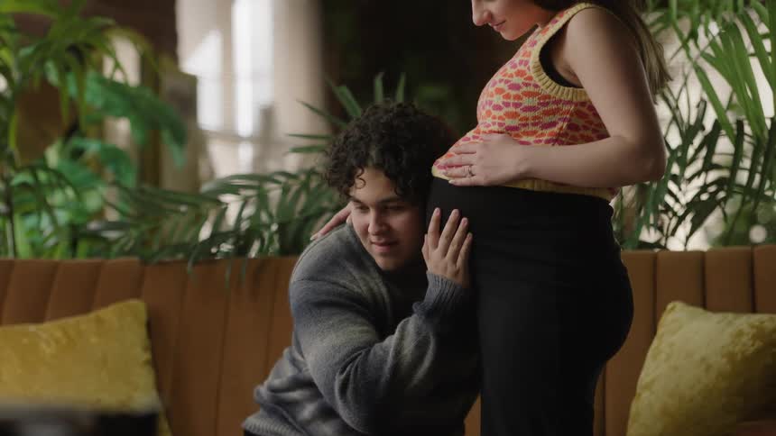 A man is on his knees listening to his wifes pregnant stomach