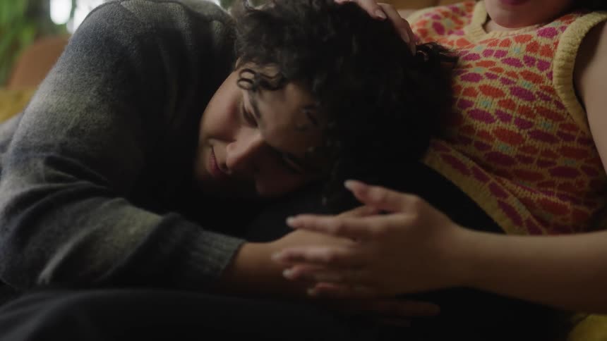 Close up of a man laying on a womans stomach as she rubs his head and the cuddle sentimentally