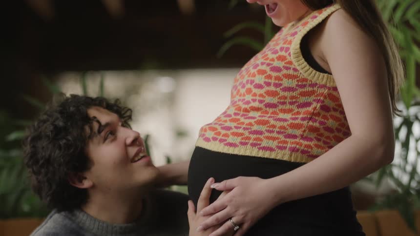A man presses his head to a pregnant womans belly as she laughs