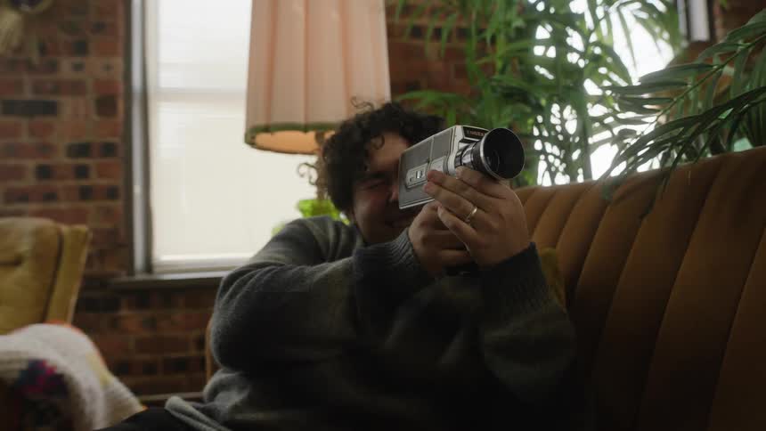 A laughing man points a camera at the woman sitting near him on the couch