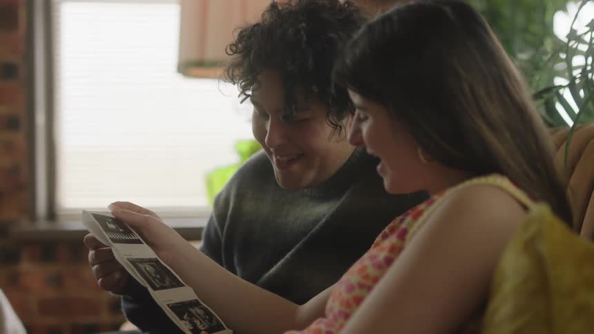 Smiling straight couple sitting on a couch looking at a baby ultrasound