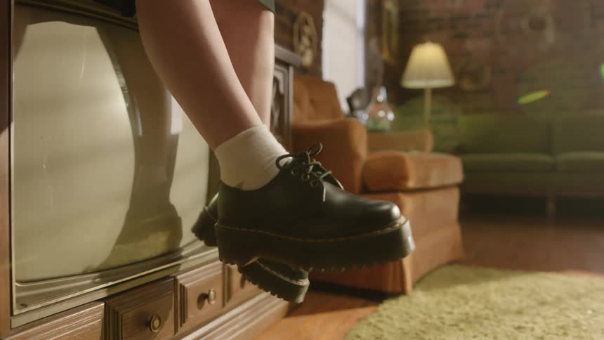 Close up of a girl sitting over a vintage television swinging her legs in the living room