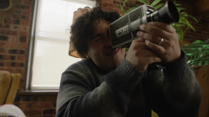A man records a woman in his apartment with a vintage camcorder