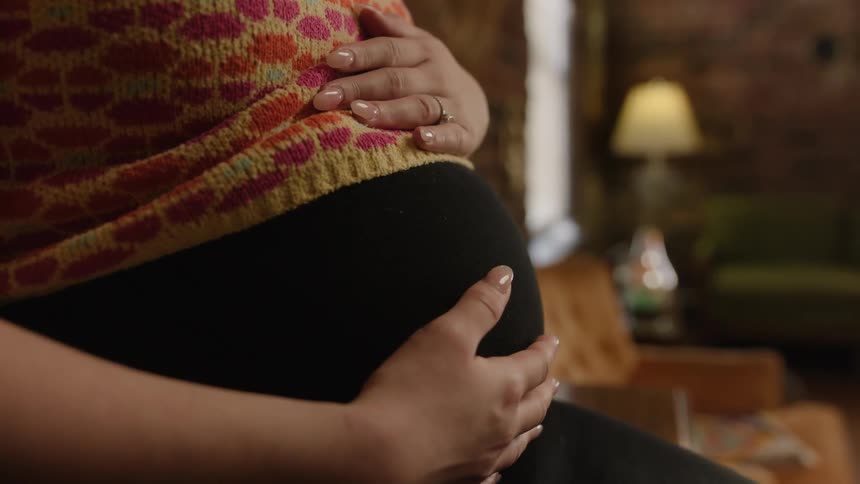 Pregnant woman seated in the living room affectionately caressing her belly