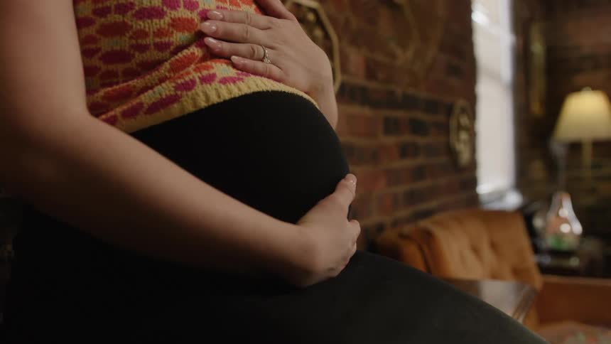 A woman sitting in a room caresses her obviously pregnant belly