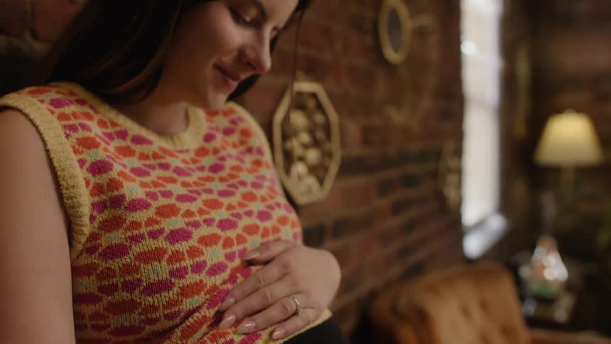 A close up of a womans face with a smile on it as she looks down while rubbing her pregnant belly