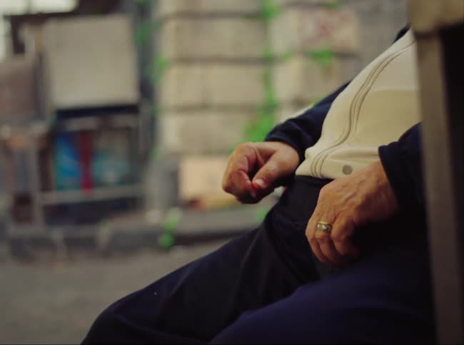 A man sitting in a public bench puts his hand down after making a gesture