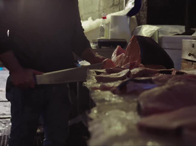 A man in an exposed and darkened building is using a cleaver to cut meat