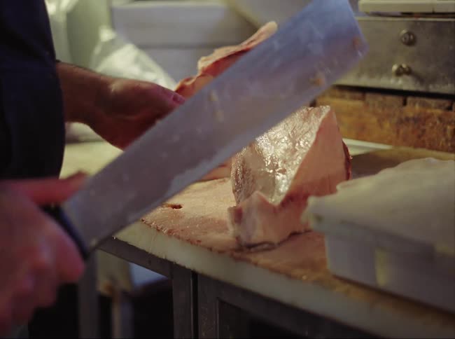 A man is using a cleaver to cut ham off the bone on a countertop