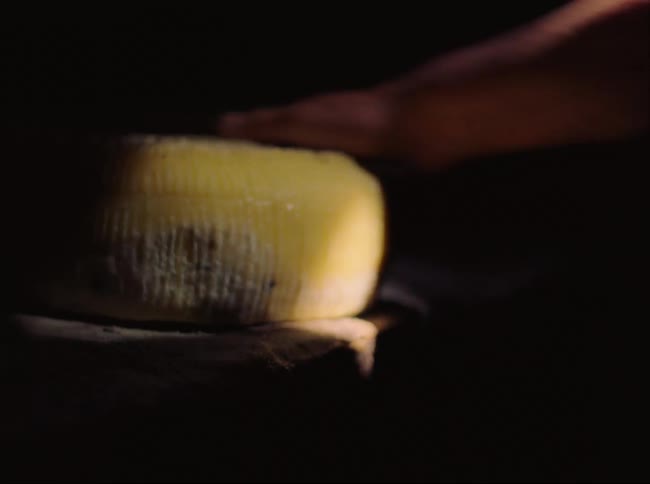 A person is flipping a cheese wheel