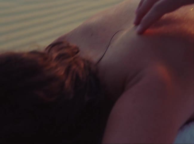 Man laying face down on a towel in the sand as a females hand runs up and down his bare back