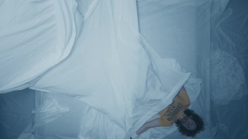 Sheet falls to cover man lying with wrapped hands on mattress