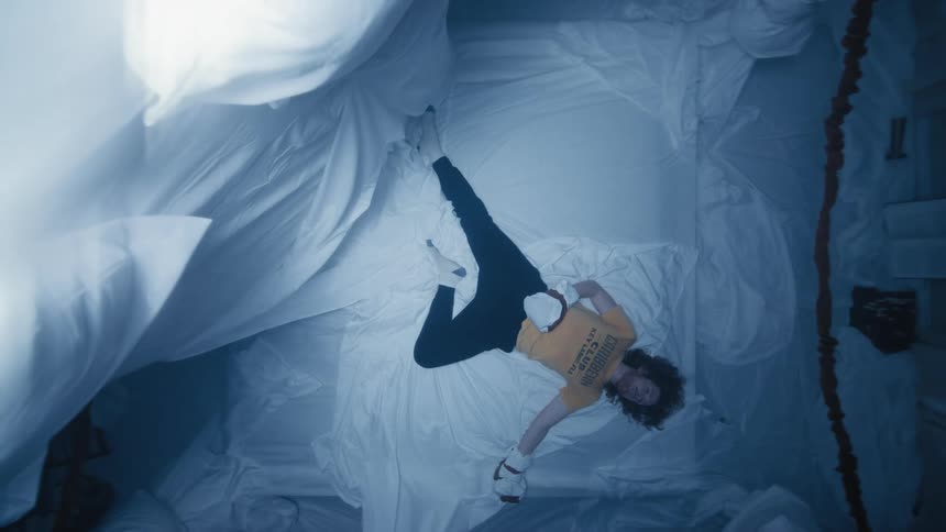 A man lies on a sheet next to a propped up mattress