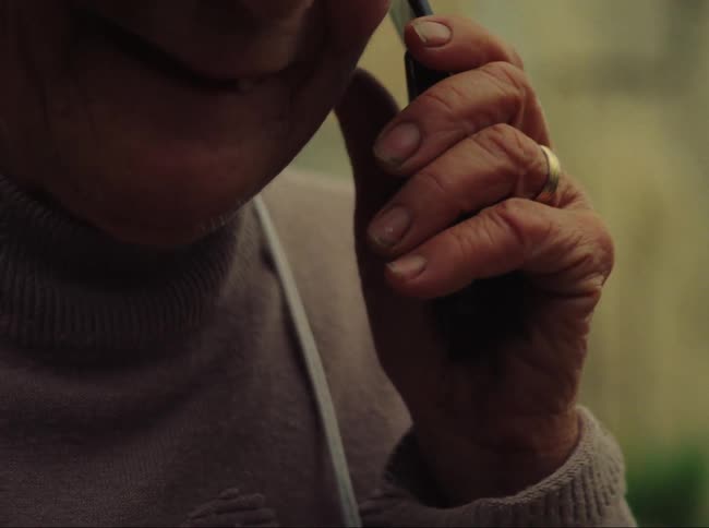 Elderly woman standing outdoors opens flip phone and holds conversation