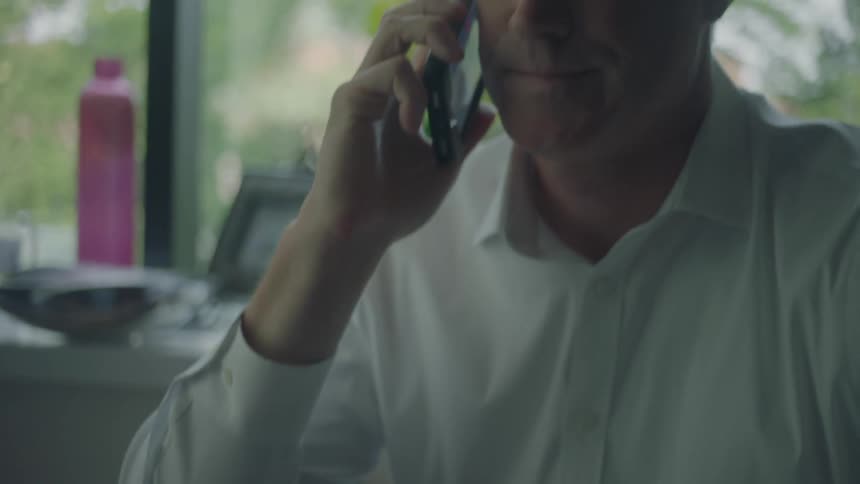 Man wearing a whiteshirt is sorting the mail when he receives a phone call with bad news