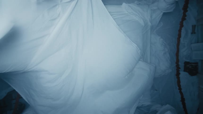 A white sheet falling on a bed