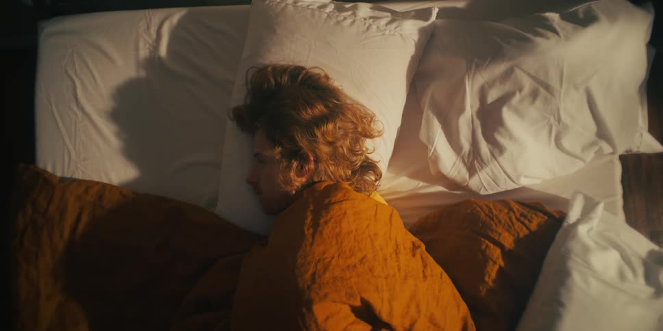 A man lying on his bed with his head on the pillow and covered by a blanket