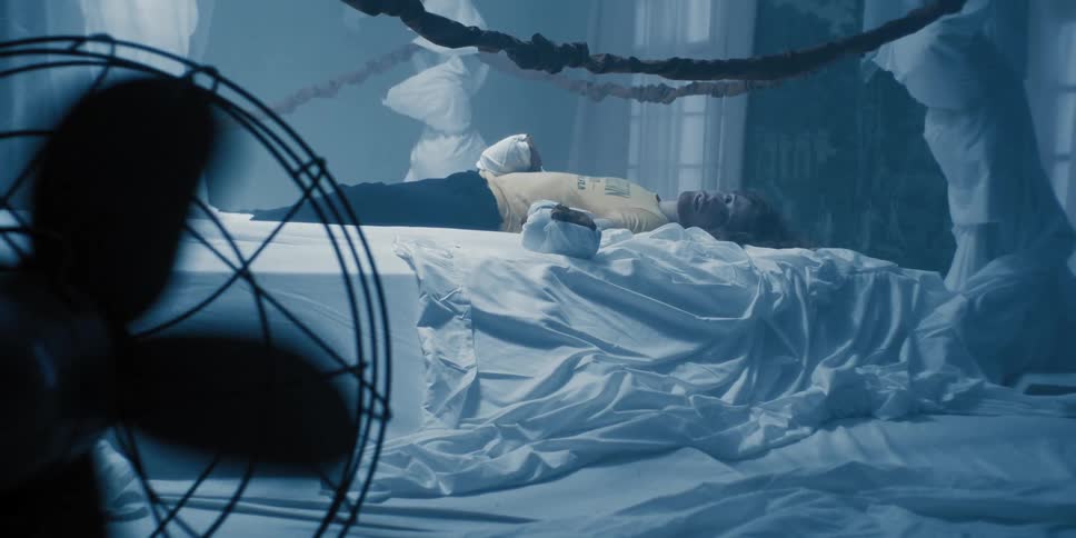 Young unconscious man laying on a disheveled bed in a room padded with white bed sheets