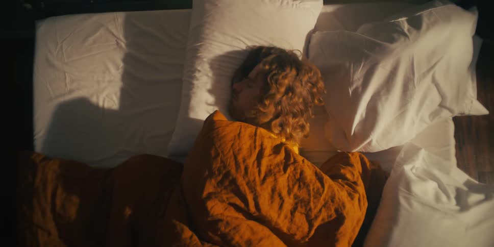 Man sleeping in his bed with an orange blanket over him as he tosses and turns