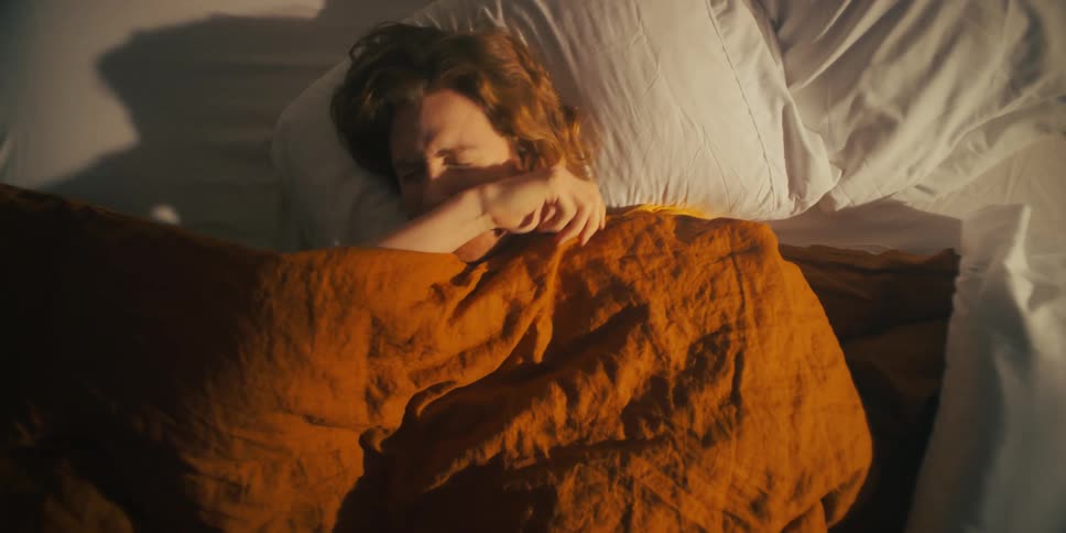 A man in bed rolls over onto his back and then onto his stomach