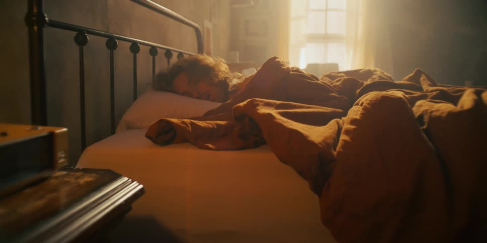 Man laying in bed with his hand outstretched before pulling it back in under the blankets
