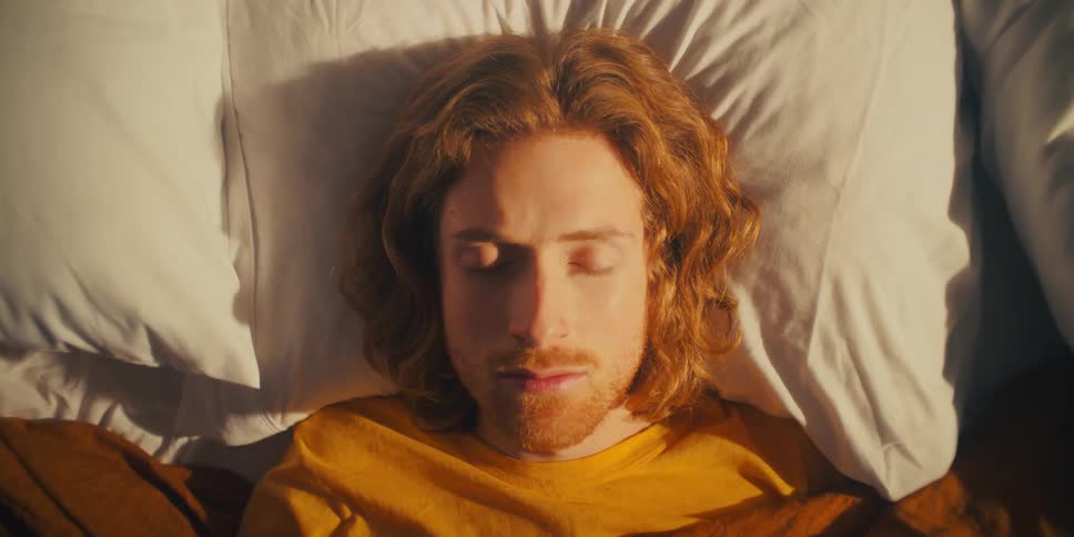 Camera zooms in on a sleeping mans face then he opens his eyes