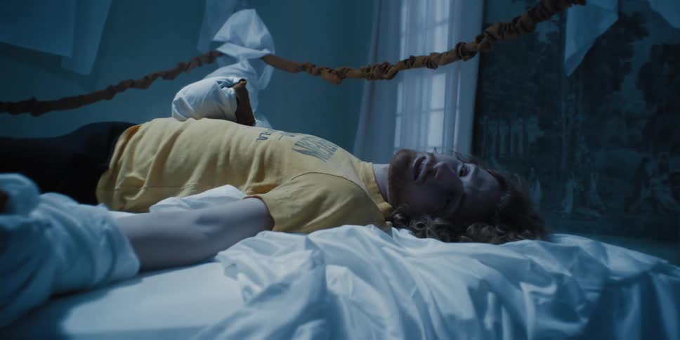 Redhead bearded man lying down as if knocked out on a boxing ring made of bed sheets