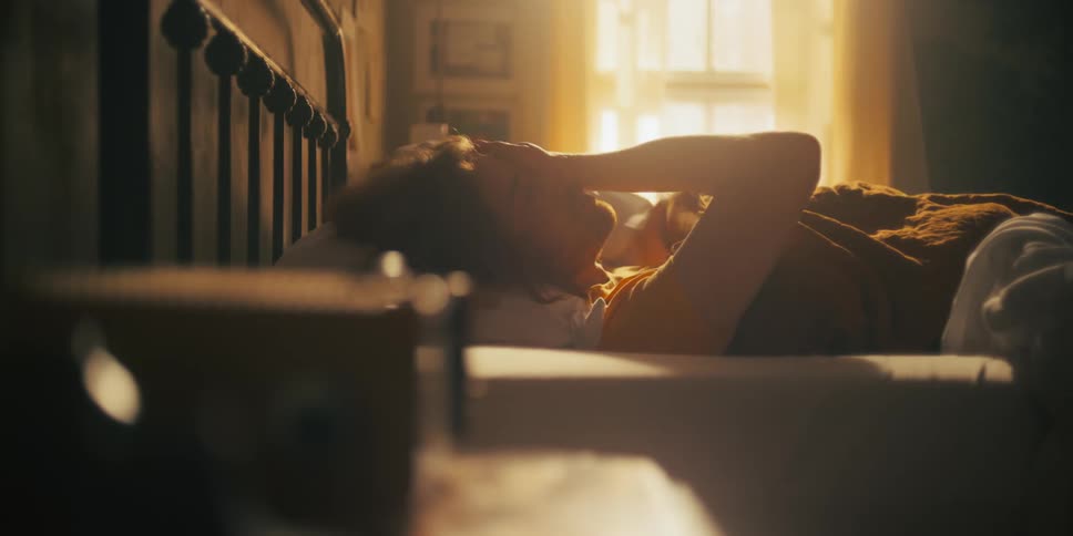 A man laying in bed pushing hair out of his face and rubbing his hands over his face