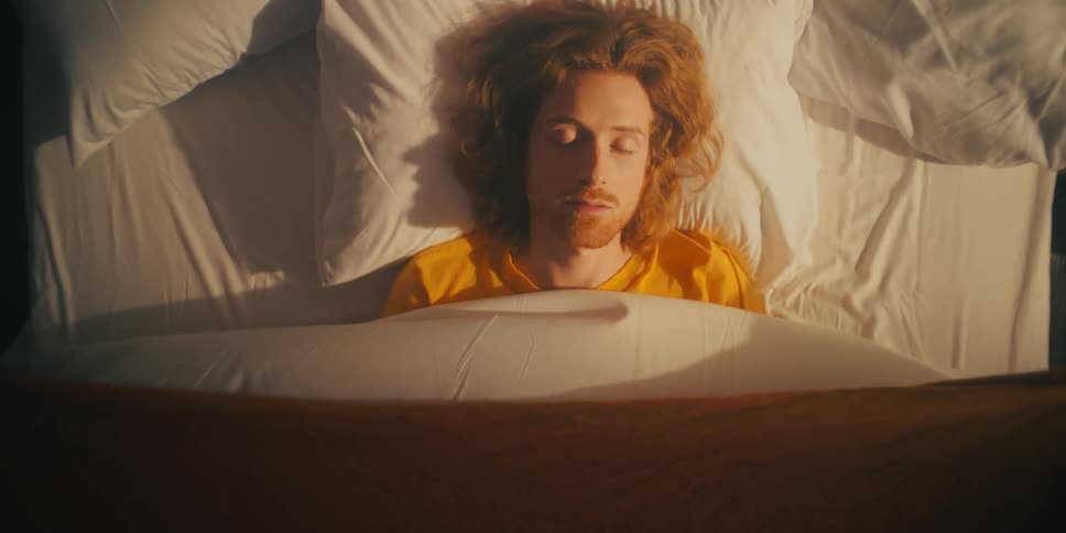 A man on a bed falls asleep as a blanket covers him as if it had a will of its own