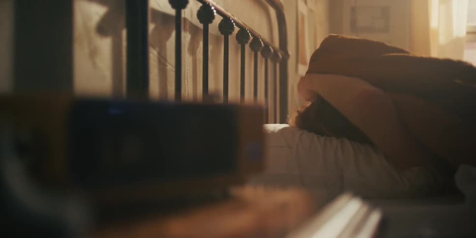 A man lying in bed during the day pulls up the bed sheets to cover his face