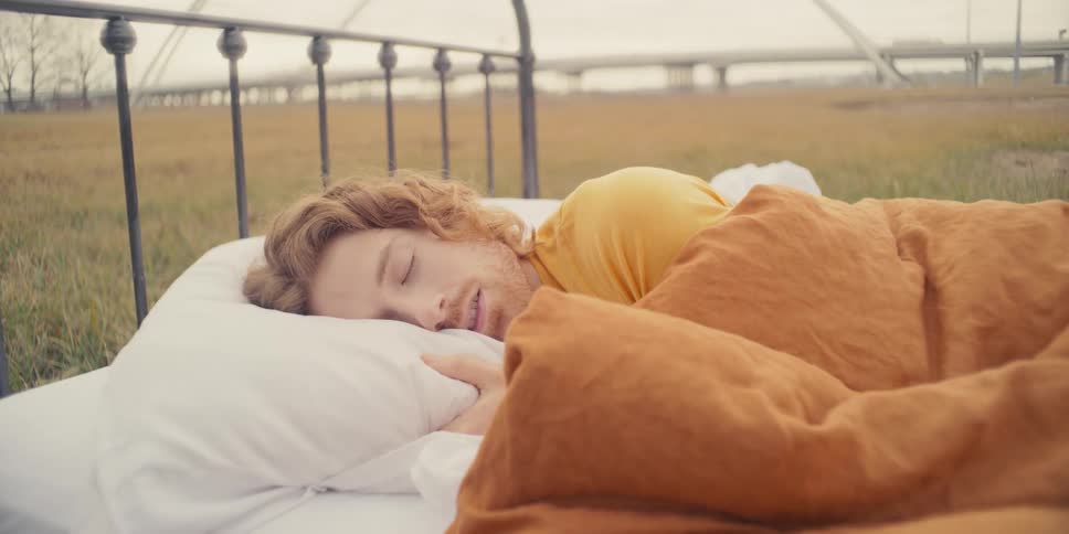 A man is asleep in his bed outside in a field