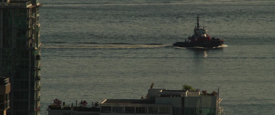 Buildings on the coast as a boat sails by leaving waves behind it
