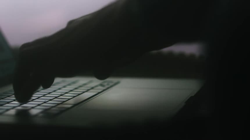 A person uses the touchpad and keyboard of a laptop in a dark room