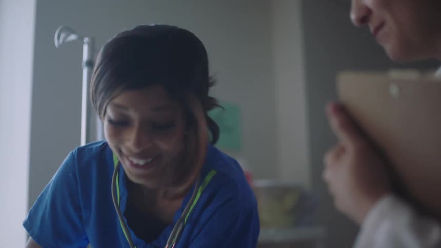 Nurse moves artificial limb on bed as doctor with clipboard talks to her