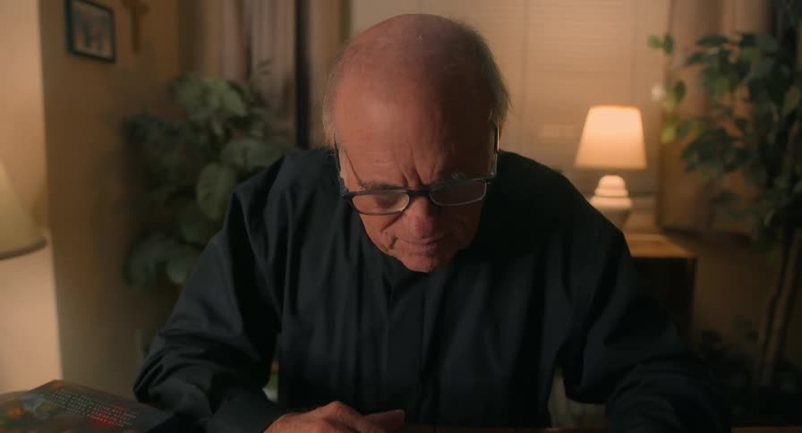 Bald elderly man wearing glasses reading a book at a table