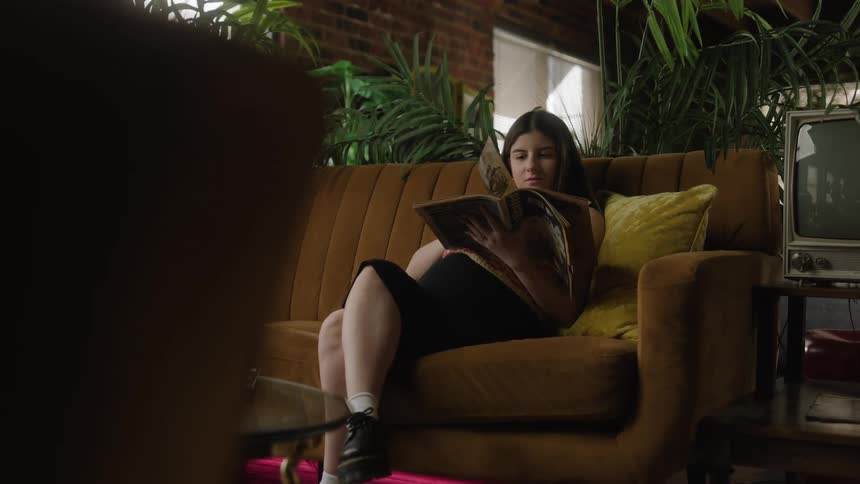 A pregnant woman flips through a magazine while sitting on a sofa indoors during the day